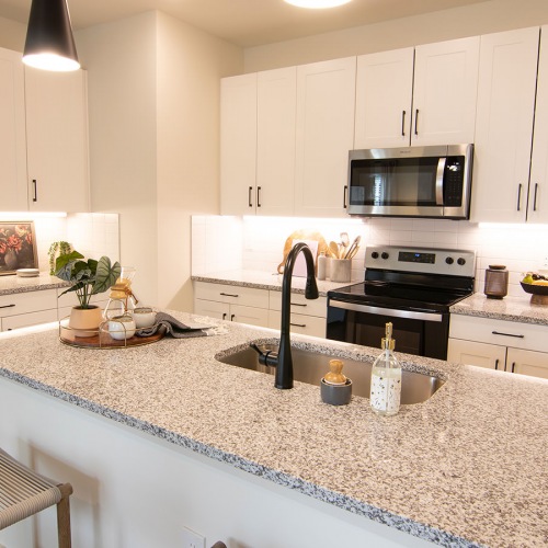 Stylish Gourmet Kitchen with Granite Countertops & Undermount Sink at Sage North Modern kitchen at Sage North apartments in White House, TN, featuring granite countertops, white shaker cabinets, stainless steel appliances, pendant lighting, and an undermount sink for a sleek, contemporary design.