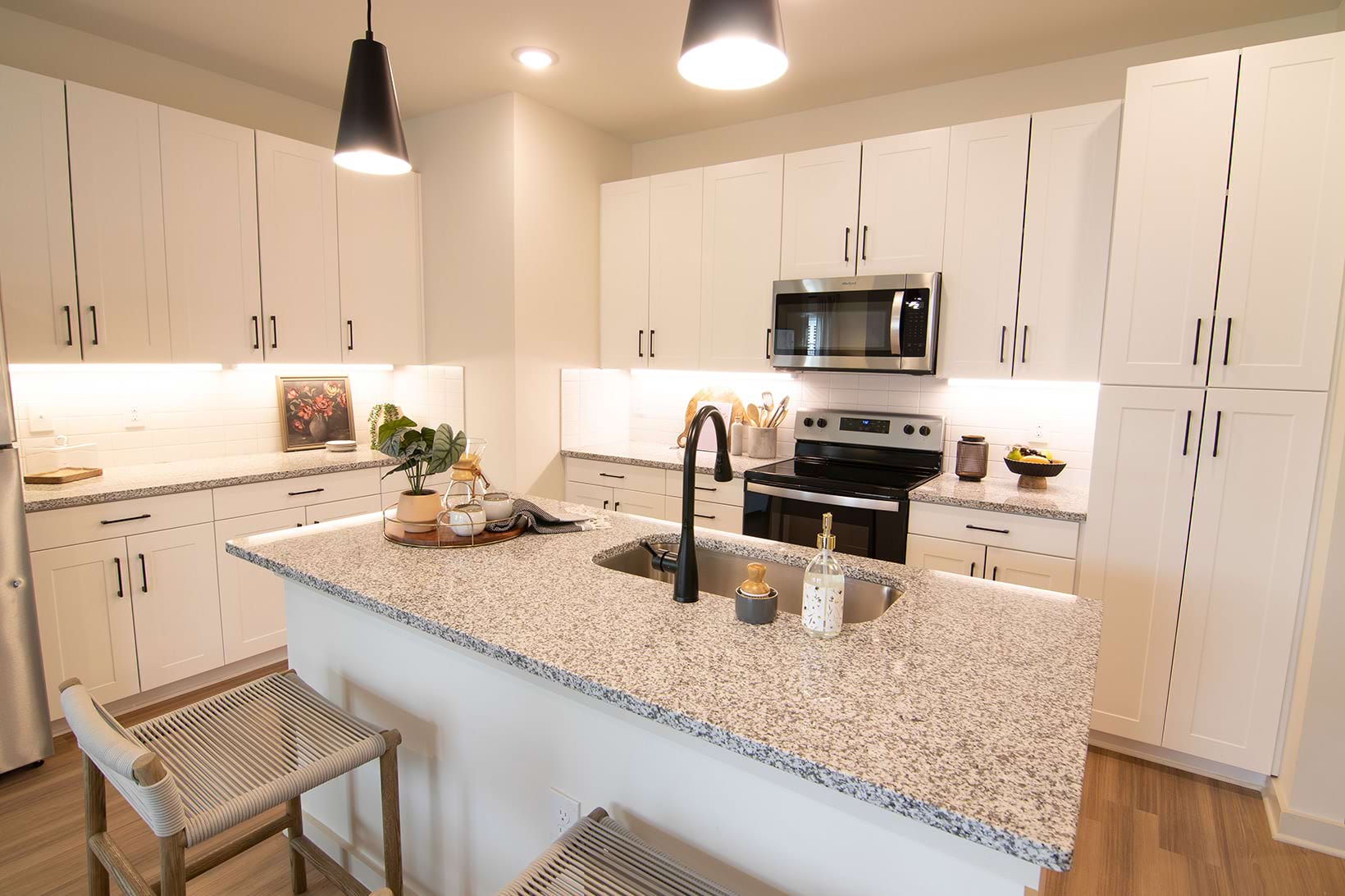 Modern kitchen at Sage North apartments in White House, TN, featuring granite countertops, white shaker cabinets, stainless steel appliances, pendant lighting, and an undermount sink for a sleek, contemporary design.
